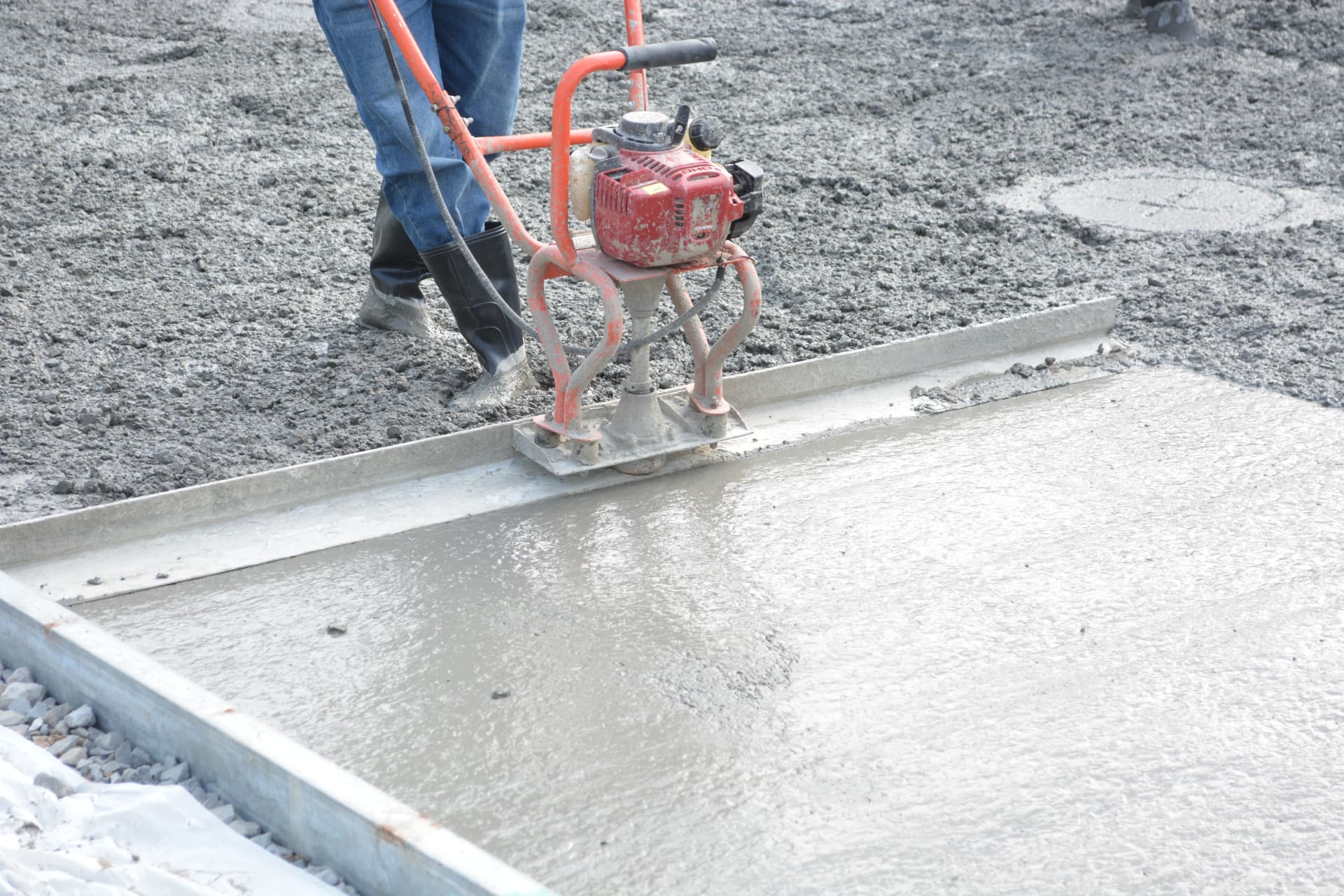 Power screed leveling a freshly poured concrete slab inside steel forms