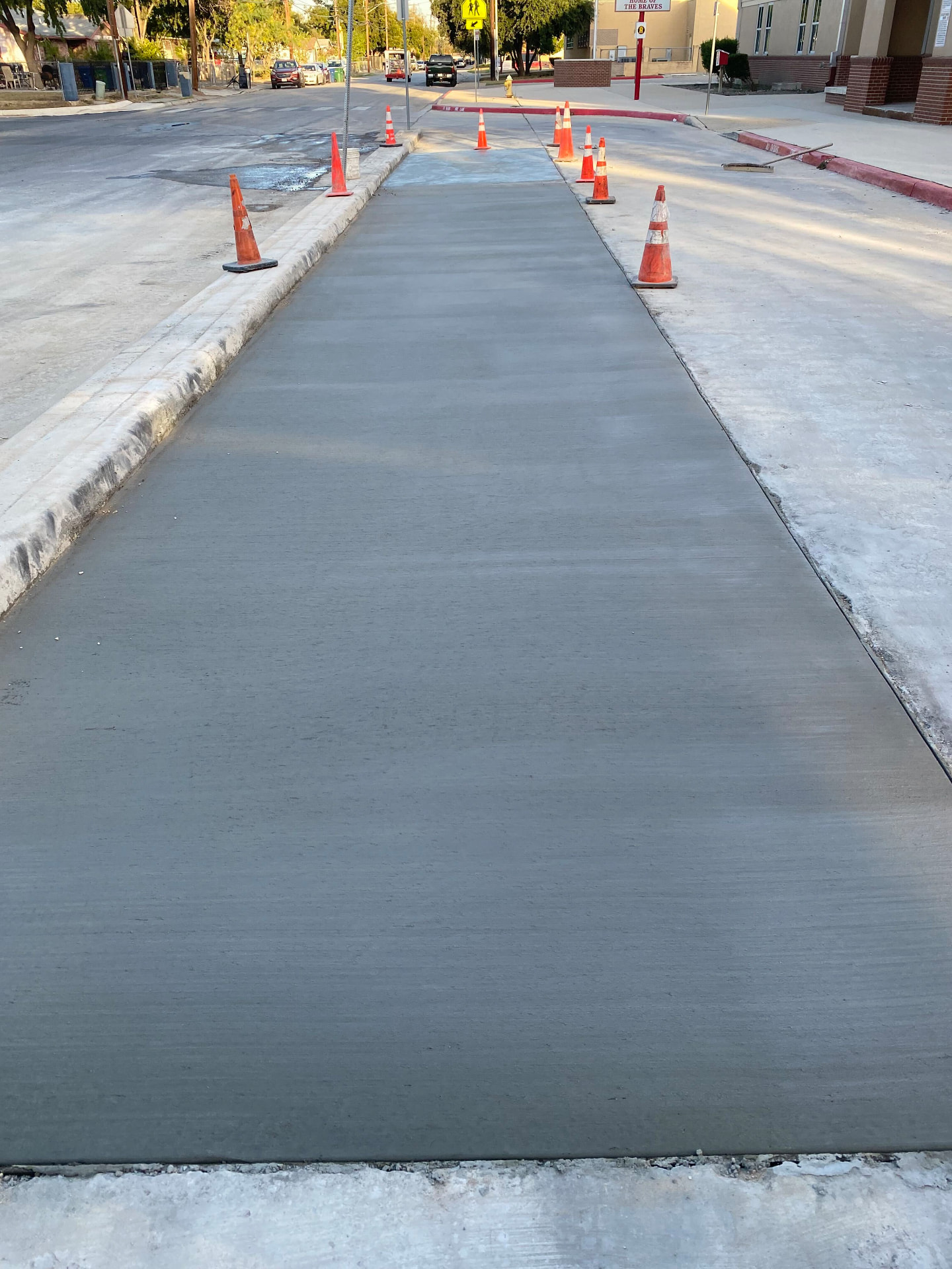 Freshly finished concrete street paving section coned off in front of a school
