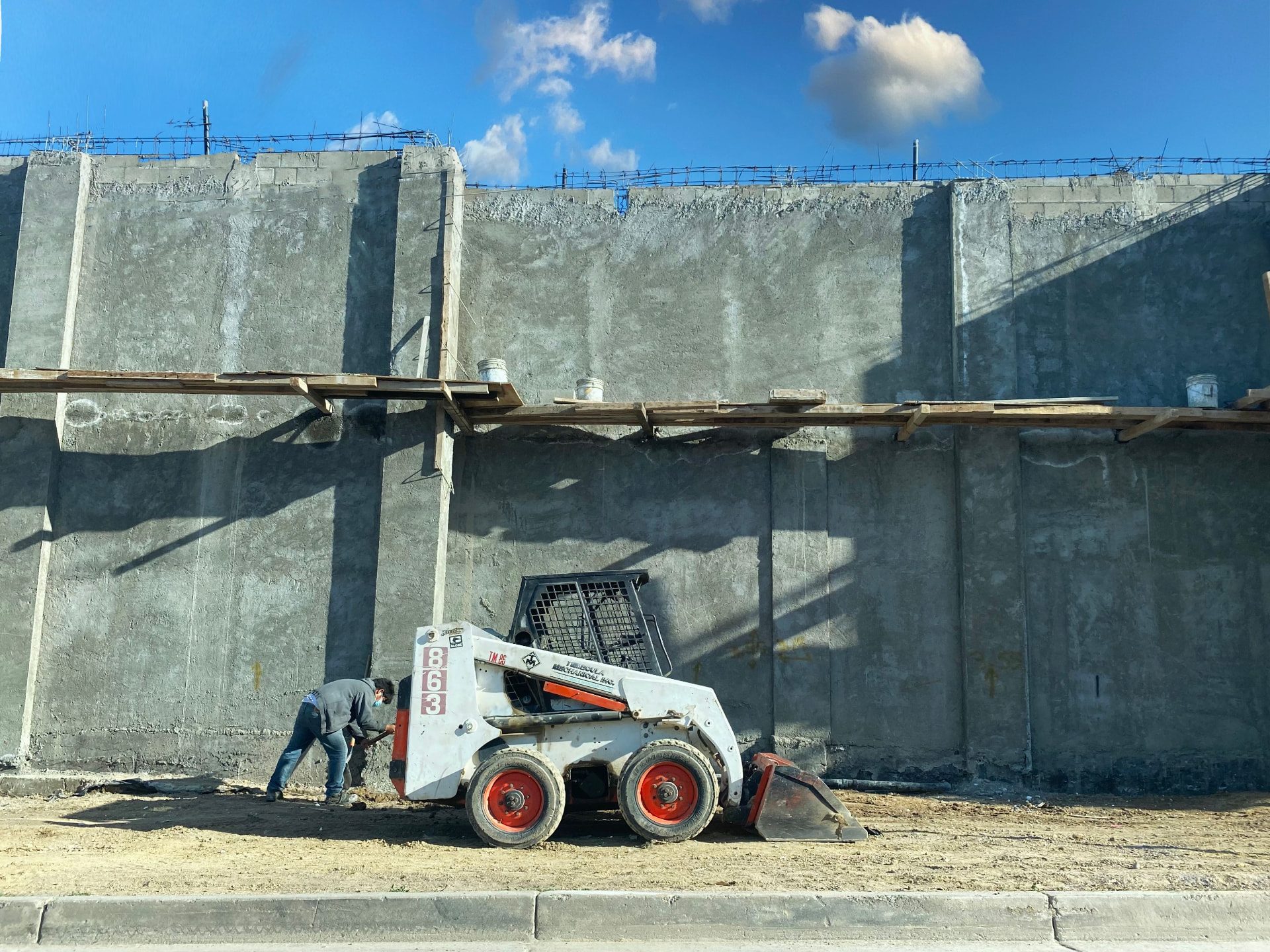 Skid steer preparing a commercial concrete site with retaining wall forms in the background